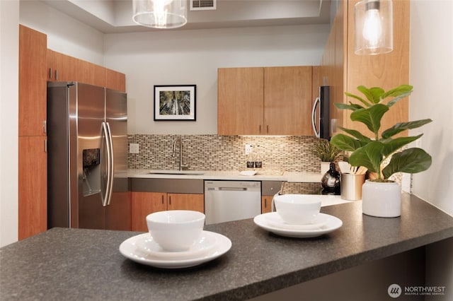 kitchen featuring appliances with stainless steel finishes, dark countertops, a sink, and tasteful backsplash