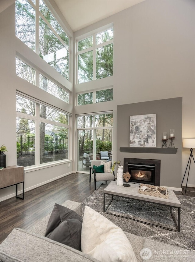 living room with wood finished floors, a glass covered fireplace, a high ceiling, and baseboards