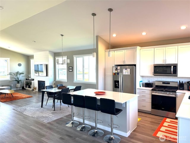 kitchen featuring a large fireplace, white cabinets, light countertops, appliances with stainless steel finishes, and tasteful backsplash