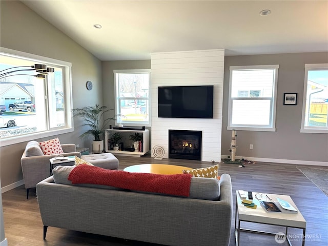 living room with a large fireplace, vaulted ceiling, baseboards, and wood finished floors