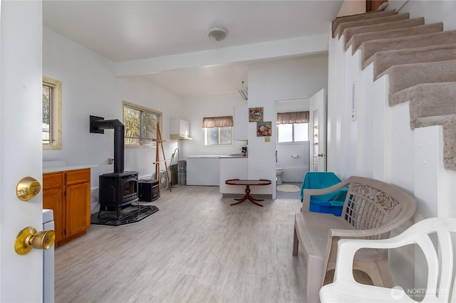 sitting room with light wood-type flooring, a wood stove, stairway, and beam ceiling