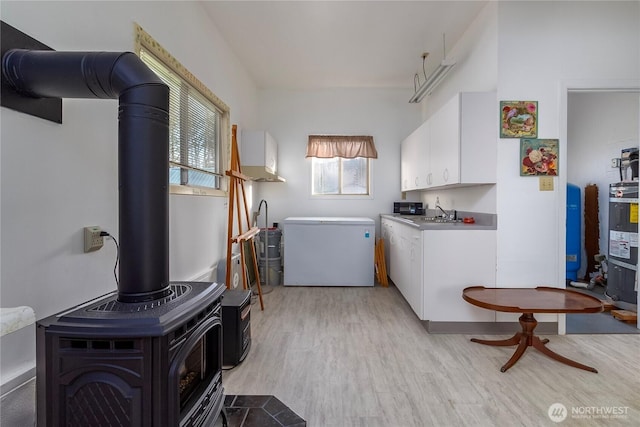 laundry area with water heater, light wood-type flooring, a sink, and a wood stove