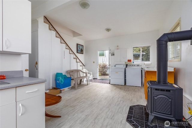 kitchen featuring washing machine and dryer, white cabinets, light countertops, light wood-type flooring, and a wood stove