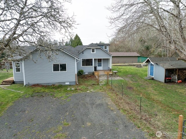 back of property with an outdoor structure, a yard, driveway, crawl space, and a storage unit