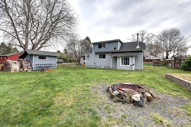 rear view of property featuring a fire pit, roof with shingles, fence, and a yard