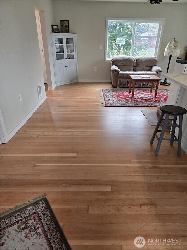 living area with light wood-type flooring, visible vents, and baseboards