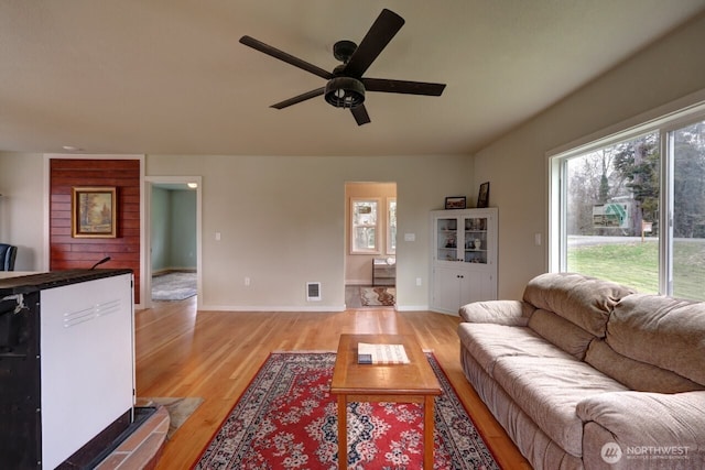 living room with light wood-style flooring, visible vents, ceiling fan, and baseboards