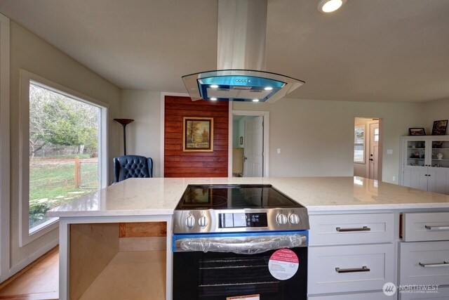 kitchen featuring electric range, island exhaust hood, white cabinetry, and light stone countertops