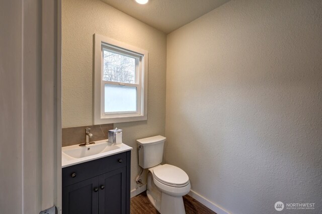 bathroom with a textured wall, toilet, wood finished floors, vanity, and baseboards