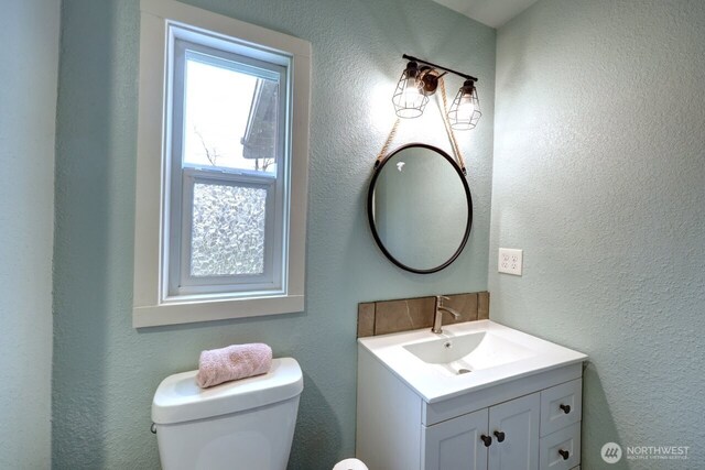 bathroom with toilet, a textured wall, and vanity