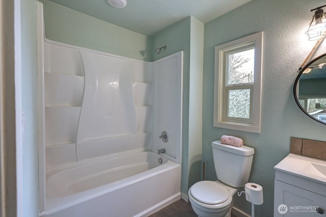 full bathroom featuring toilet, a textured wall,  shower combination, and vanity