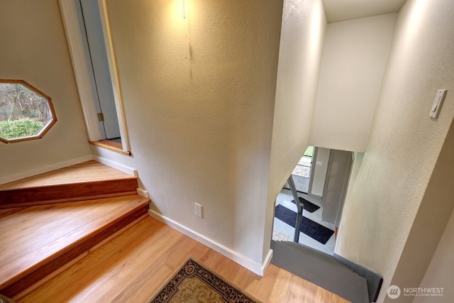 stairs with baseboards, wood finished floors, and a textured wall