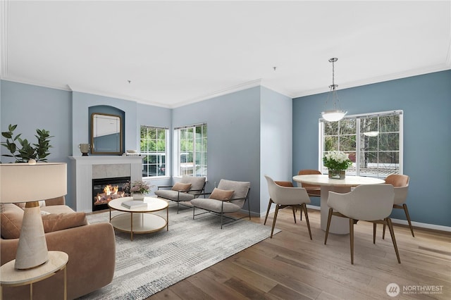 living area featuring crown molding, a glass covered fireplace, wood finished floors, and baseboards