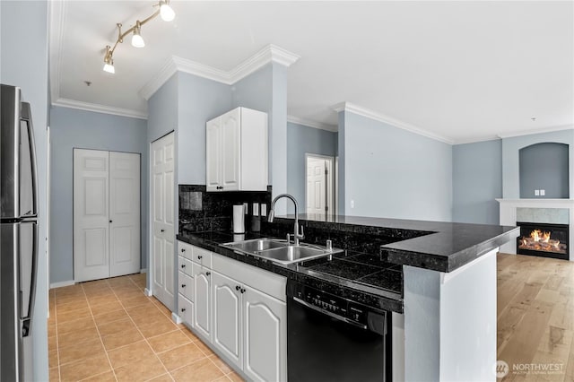 kitchen with a warm lit fireplace, a peninsula, a sink, freestanding refrigerator, and dishwasher