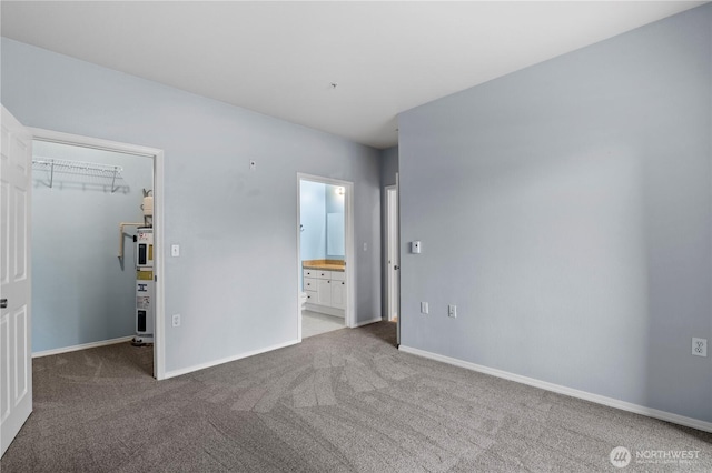 unfurnished bedroom featuring a walk in closet, carpet flooring, and baseboards