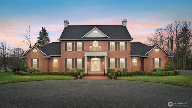 colonial house with brick siding, a chimney, and a front lawn