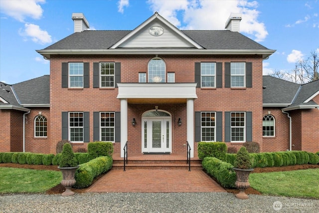 colonial-style house featuring a shingled roof, brick siding, and a chimney