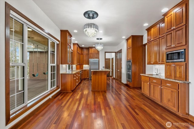 kitchen featuring a sink, an inviting chandelier, dark wood-style flooring, light stone counters, and appliances with stainless steel finishes