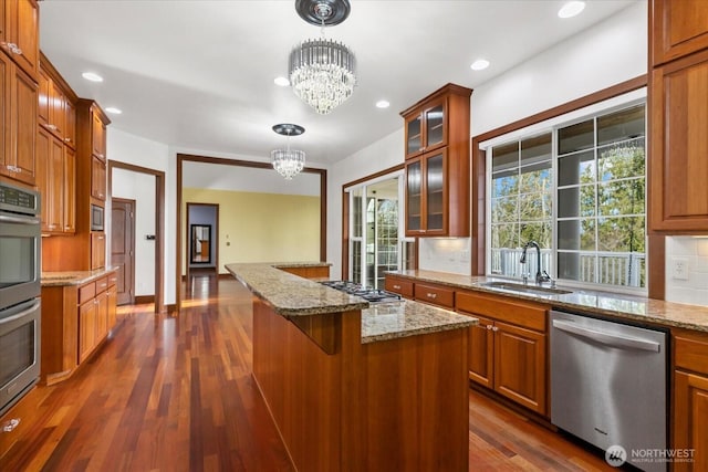 kitchen with a chandelier, brown cabinetry, appliances with stainless steel finishes, backsplash, and a sink
