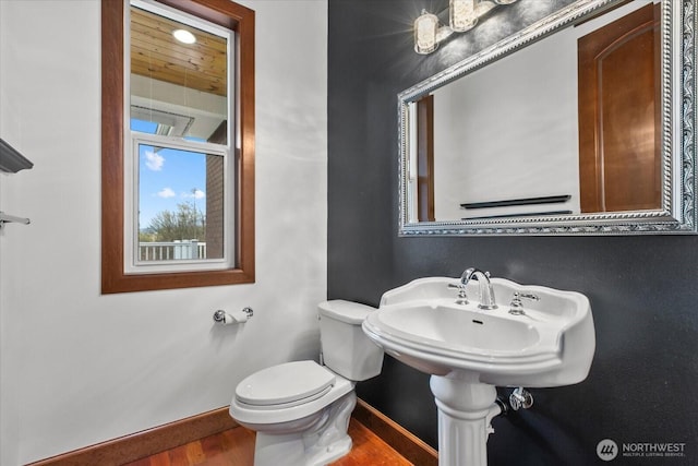 half bathroom with wood finished floors, toilet, and baseboards