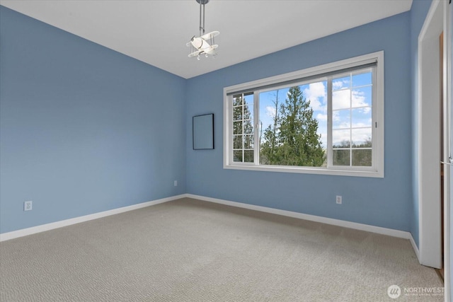 spare room featuring a chandelier, carpet flooring, and baseboards