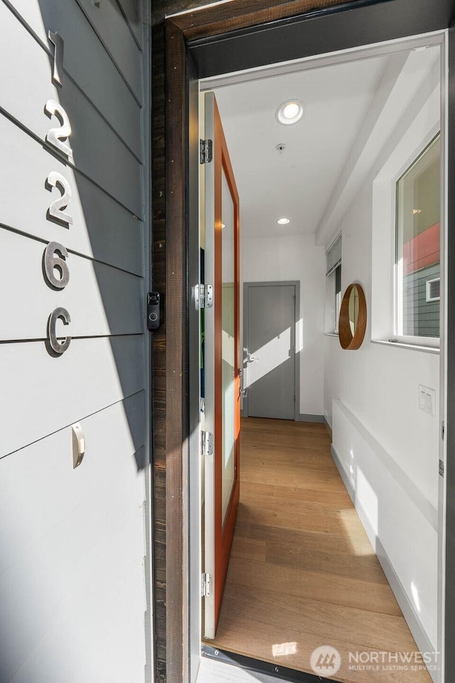 hallway featuring baseboards, light wood finished floors, and recessed lighting