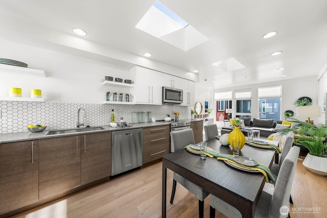 kitchen with a skylight, stainless steel appliances, white cabinetry, open shelves, and a sink