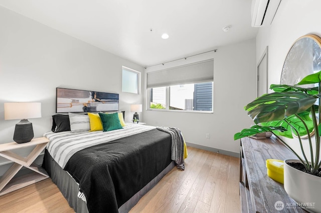 bedroom with baseboards, hardwood / wood-style floors, and a wall mounted AC