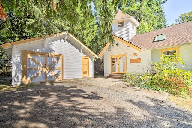 view of front of property featuring an outbuilding, french doors, a detached garage, a shingled roof, and driveway