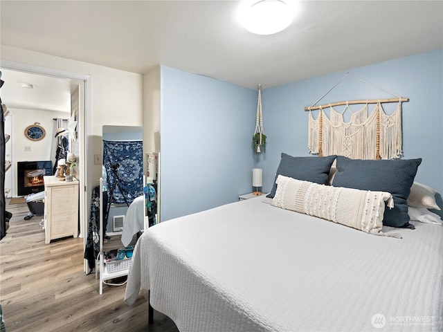 bedroom with a warm lit fireplace and light wood finished floors