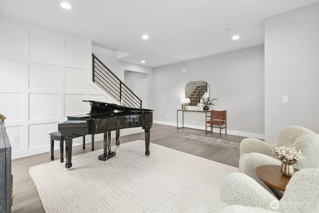 living area with baseboards, wood finished floors, stairs, a decorative wall, and recessed lighting