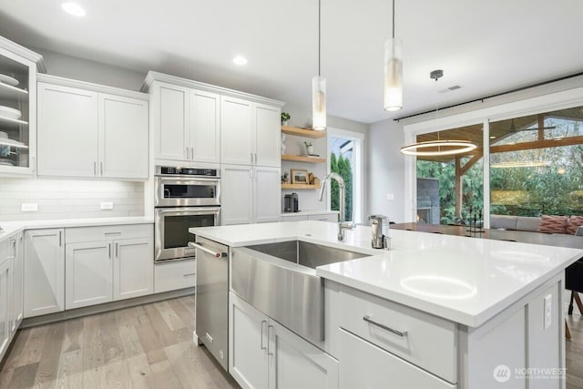 kitchen featuring white cabinets, decorative backsplash, stainless steel appliances, light countertops, and light wood-style floors