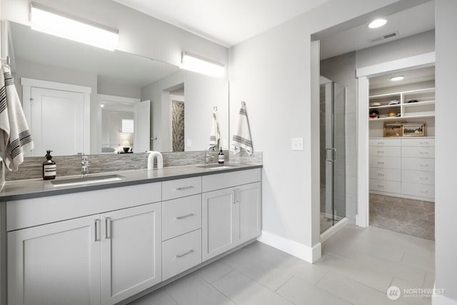 full bath with double vanity, visible vents, a sink, a shower stall, and baseboards