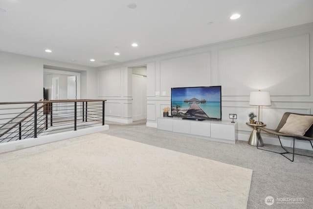 living area with light carpet, a decorative wall, crown molding, and recessed lighting