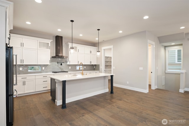 kitchen featuring wall chimney range hood, a breakfast bar area, light countertops, freestanding refrigerator, and gas cooktop