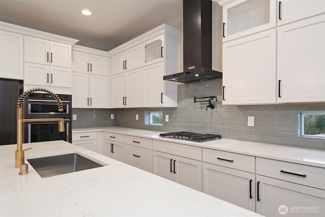 kitchen with a sink, refrigerator, white cabinetry, stainless steel gas stovetop, and wall chimney range hood