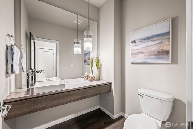 bathroom featuring toilet, wood finished floors, baseboards, and a sink