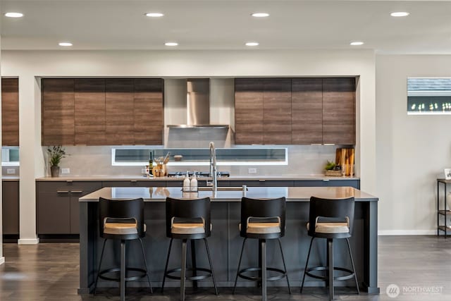 kitchen with decorative backsplash, a breakfast bar area, modern cabinets, and wall chimney range hood