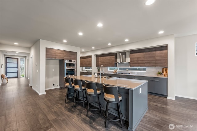 kitchen with a kitchen breakfast bar, modern cabinets, wall chimney exhaust hood, and a sink