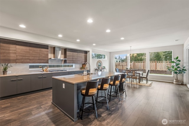 kitchen featuring modern cabinets, gray cabinets, a sink, a kitchen breakfast bar, and wall chimney range hood