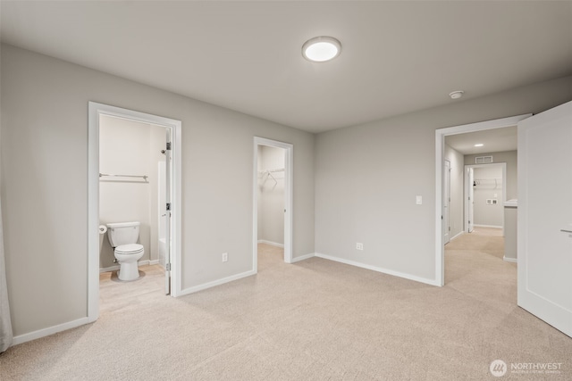 unfurnished bedroom featuring a walk in closet, light carpet, visible vents, connected bathroom, and baseboards