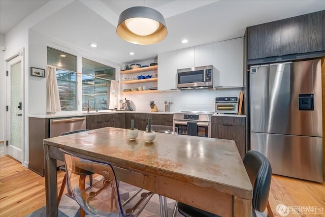 kitchen featuring stainless steel appliances, modern cabinets, light wood finished floors, and tasteful backsplash