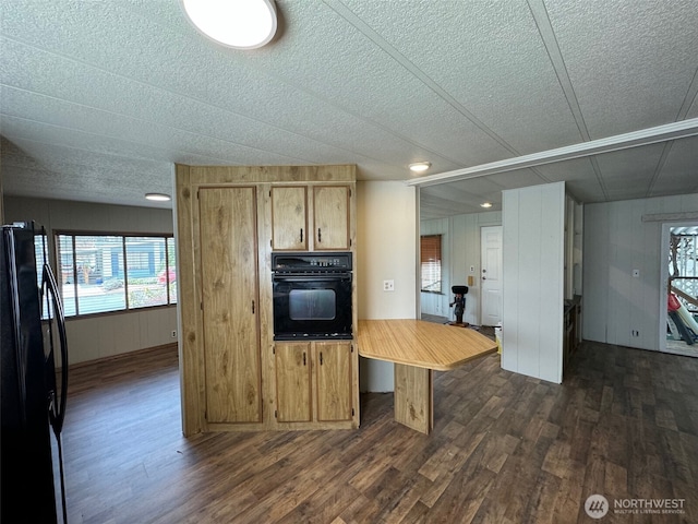 kitchen featuring a textured ceiling, black appliances, dark wood-type flooring, and light countertops