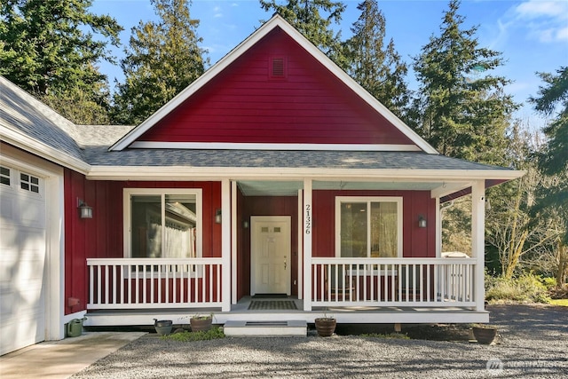 view of front of home with covered porch, a garage, and roof with shingles