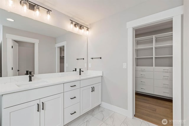 bathroom featuring marble finish floor, a spacious closet, double vanity, and a sink