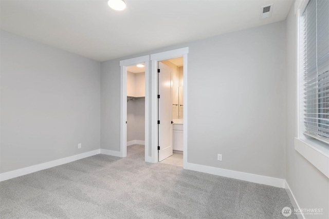 unfurnished bedroom featuring a walk in closet, a closet, visible vents, light carpet, and baseboards