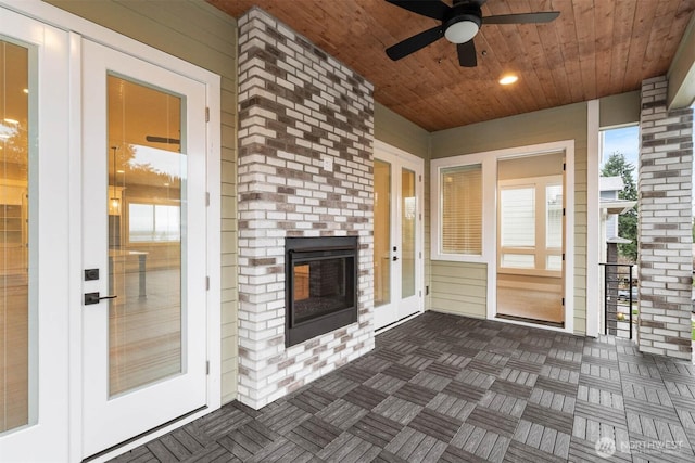 unfurnished sunroom featuring wood ceiling, a ceiling fan, and an outdoor brick fireplace