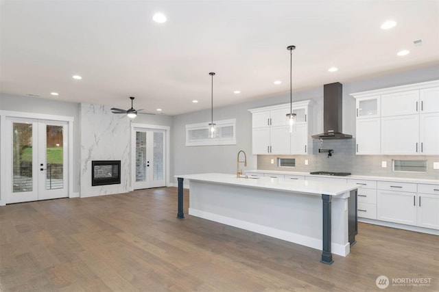 kitchen with a fireplace, a sink, gas stovetop, french doors, and wall chimney exhaust hood