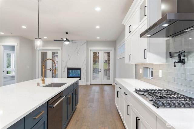 kitchen featuring french doors, appliances with stainless steel finishes, white cabinets, a sink, and wall chimney range hood