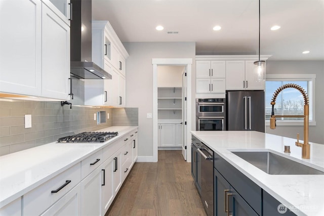 kitchen featuring dark wood-style flooring, appliances with stainless steel finishes, white cabinetry, a sink, and wall chimney range hood